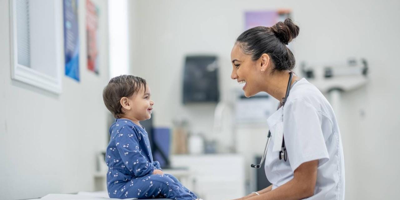 Nurse talking to smiling toddler on exam table