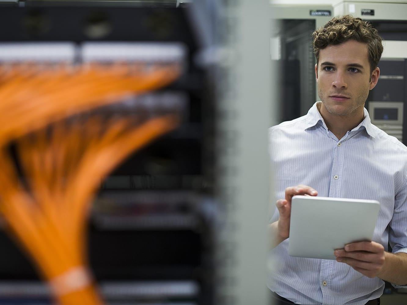 Data center technician using digital tablet performing maintenance check of mainframe equipment  