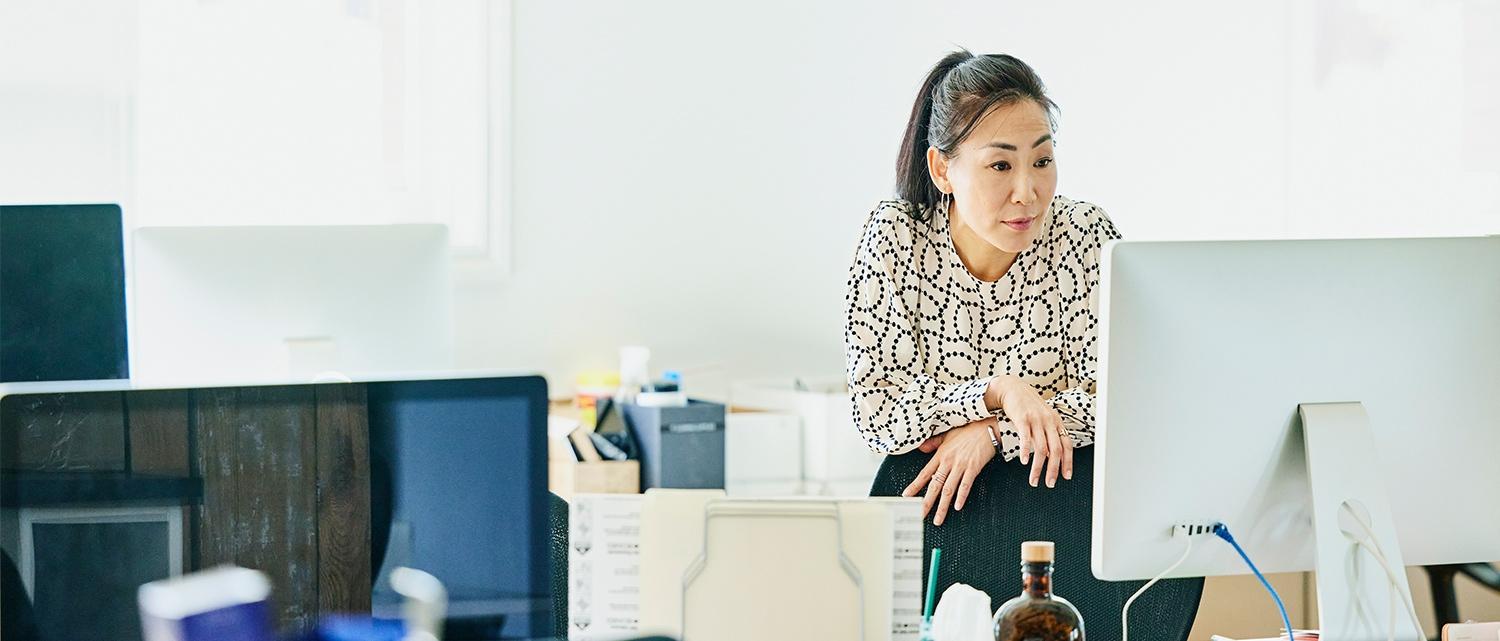 Business woman standing up at desk looking at computer monitor