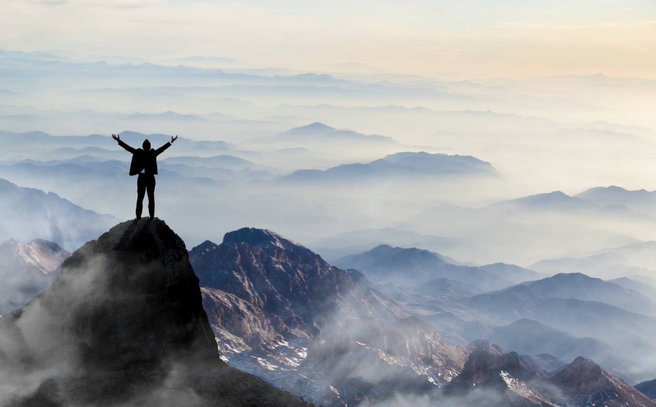 Person on a mountaintop celebrates with arms raised.