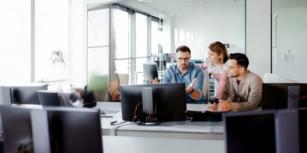 Three coworkers in discussion at desktop computer