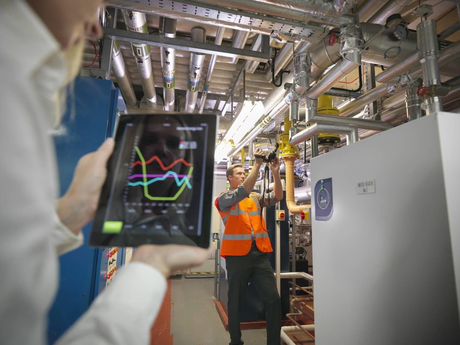 Workers using tablet in boiler room to check efficiency of office heating