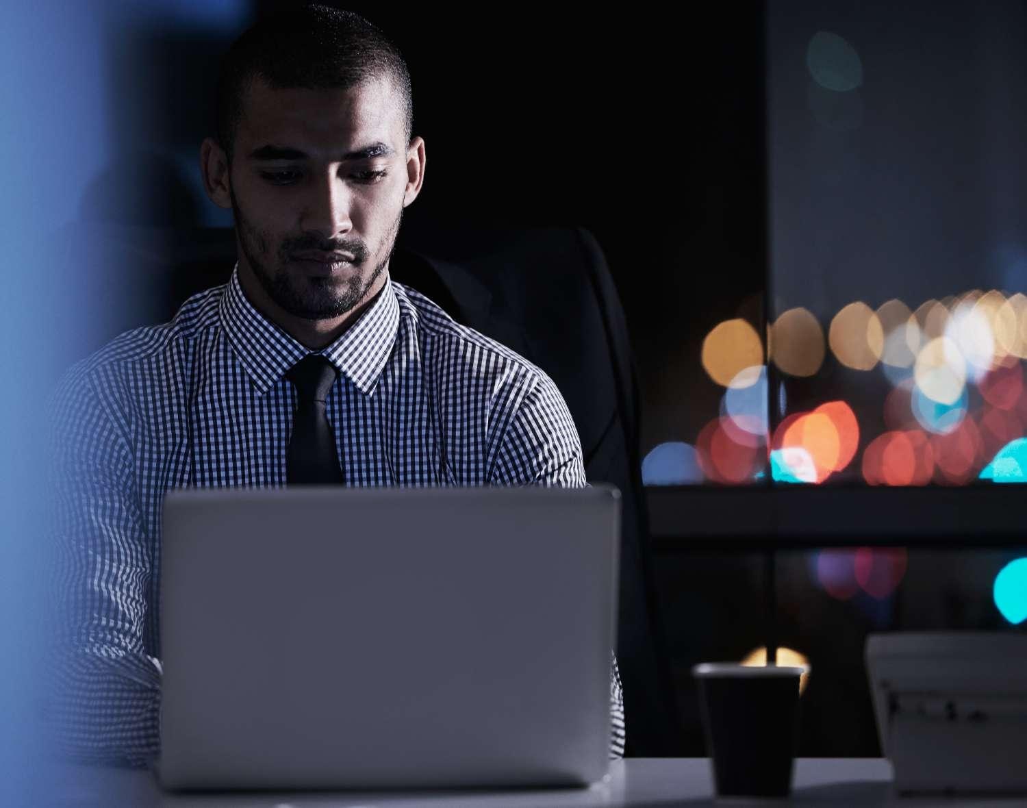 Man with a tie works on a laptop at night