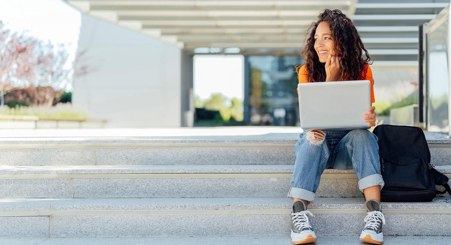 Woman sitting on steps with laptop and smiling