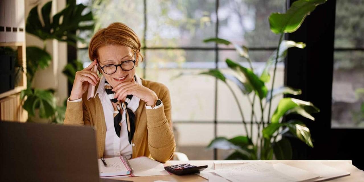 Woman talking on phone at laptop using calculator