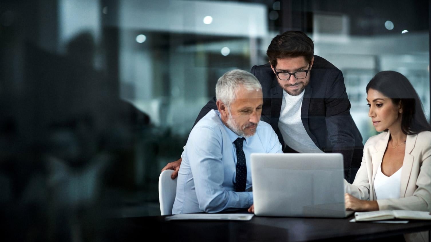 Three colleagues gather around a laptop