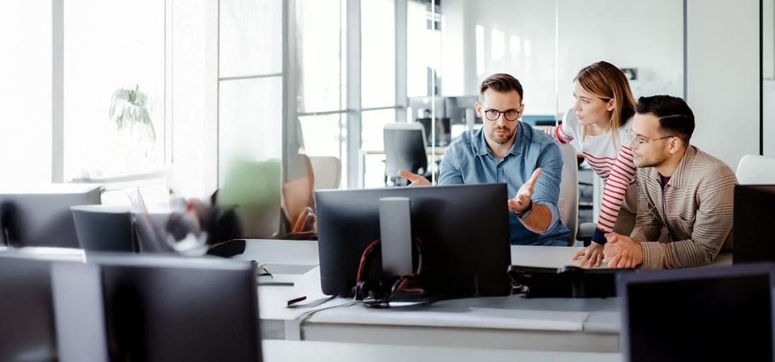 Three coworkers in discussion at desktop computer in office