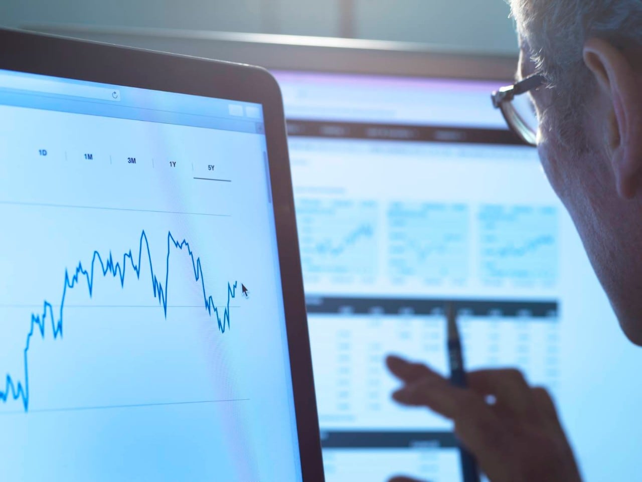 A tightly cropped photo of a man wearing glasses looking at a line graph on a laptop screen