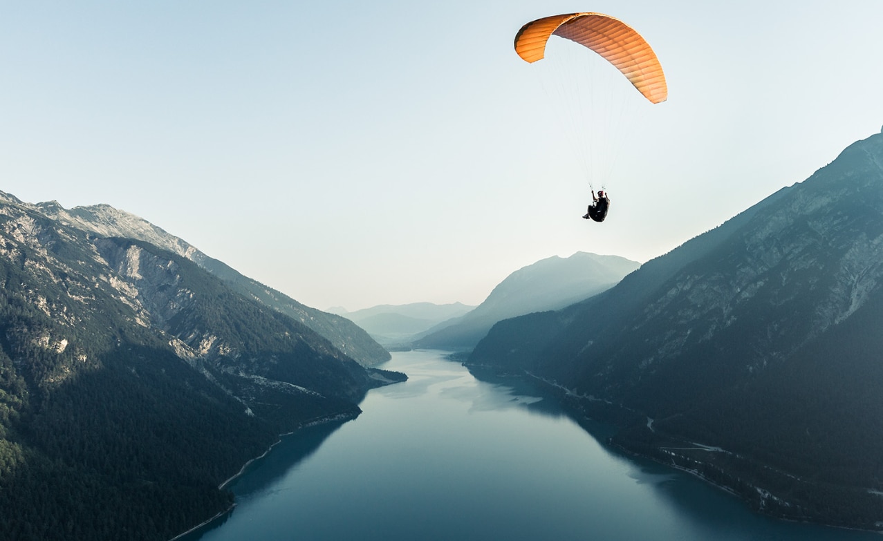 Paraglider over smooth lake surrounded by mountains
