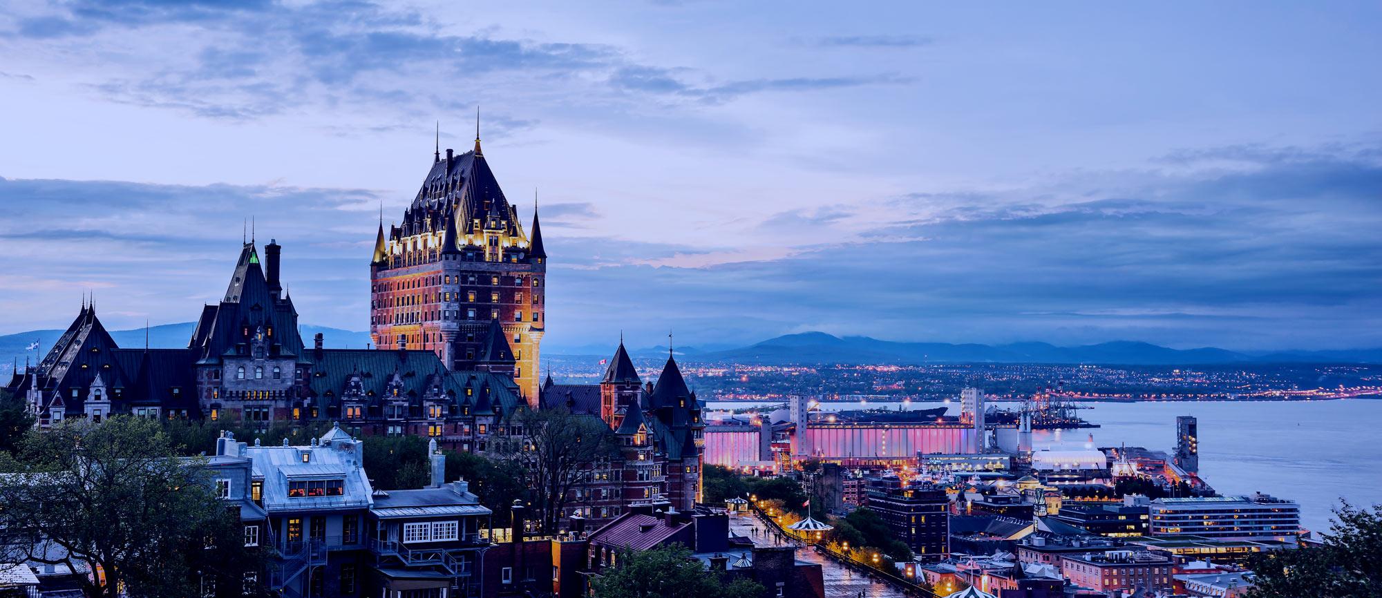 Cityscape or skyline of Quebec City, Canada, Chateau Frontenac, park and old town streets during sunset with illuminated castle, red Espace 400e building
