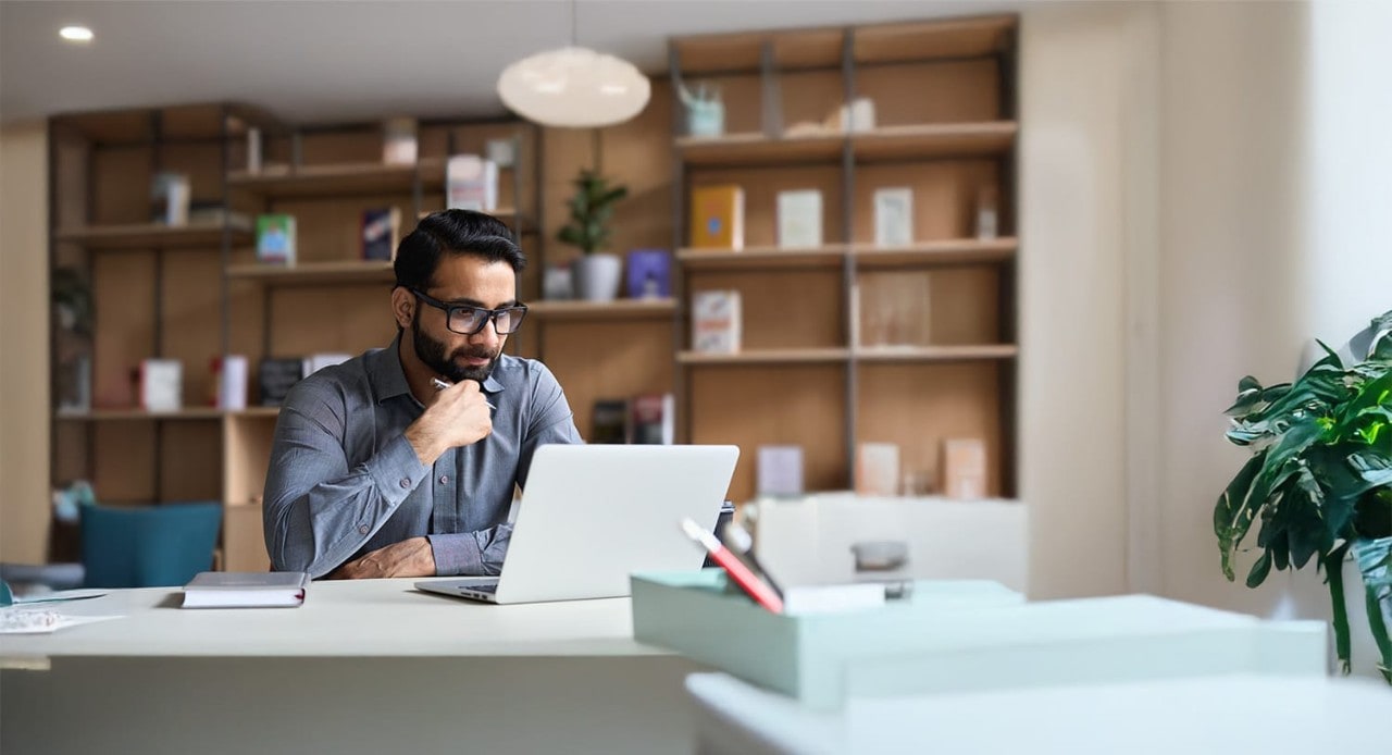 Indian male with glasses using laptop in modern office