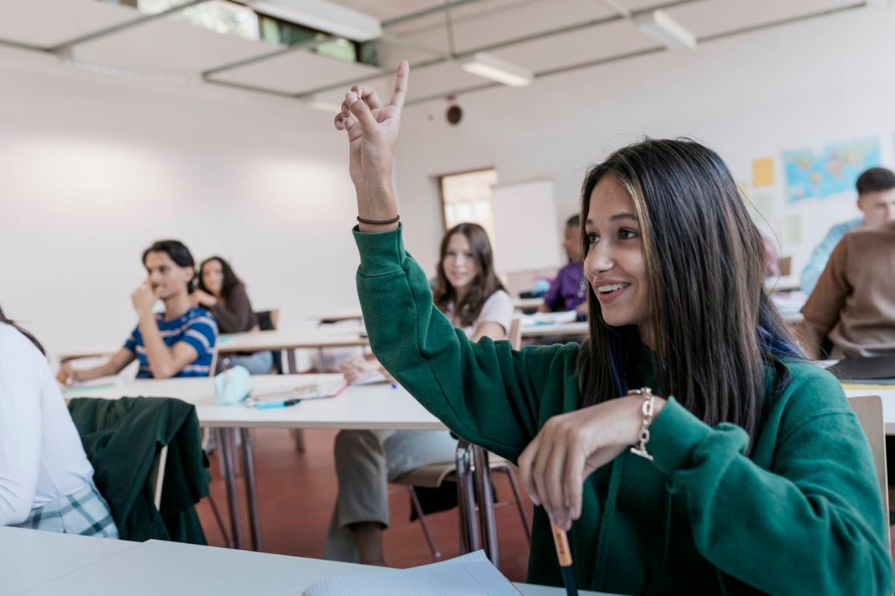 Young girl raising hand and smiling in classroom