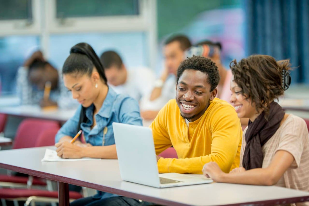 College students gathered around a laptop, smiling