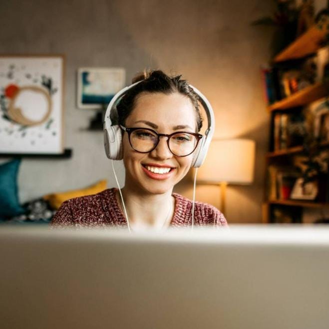 Woman in headphones smiling at computer monitor